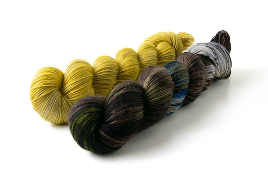 Two skeins of yarn next to each other. One is a moody variegate with a brown base and the other is a cool yellow tonal.