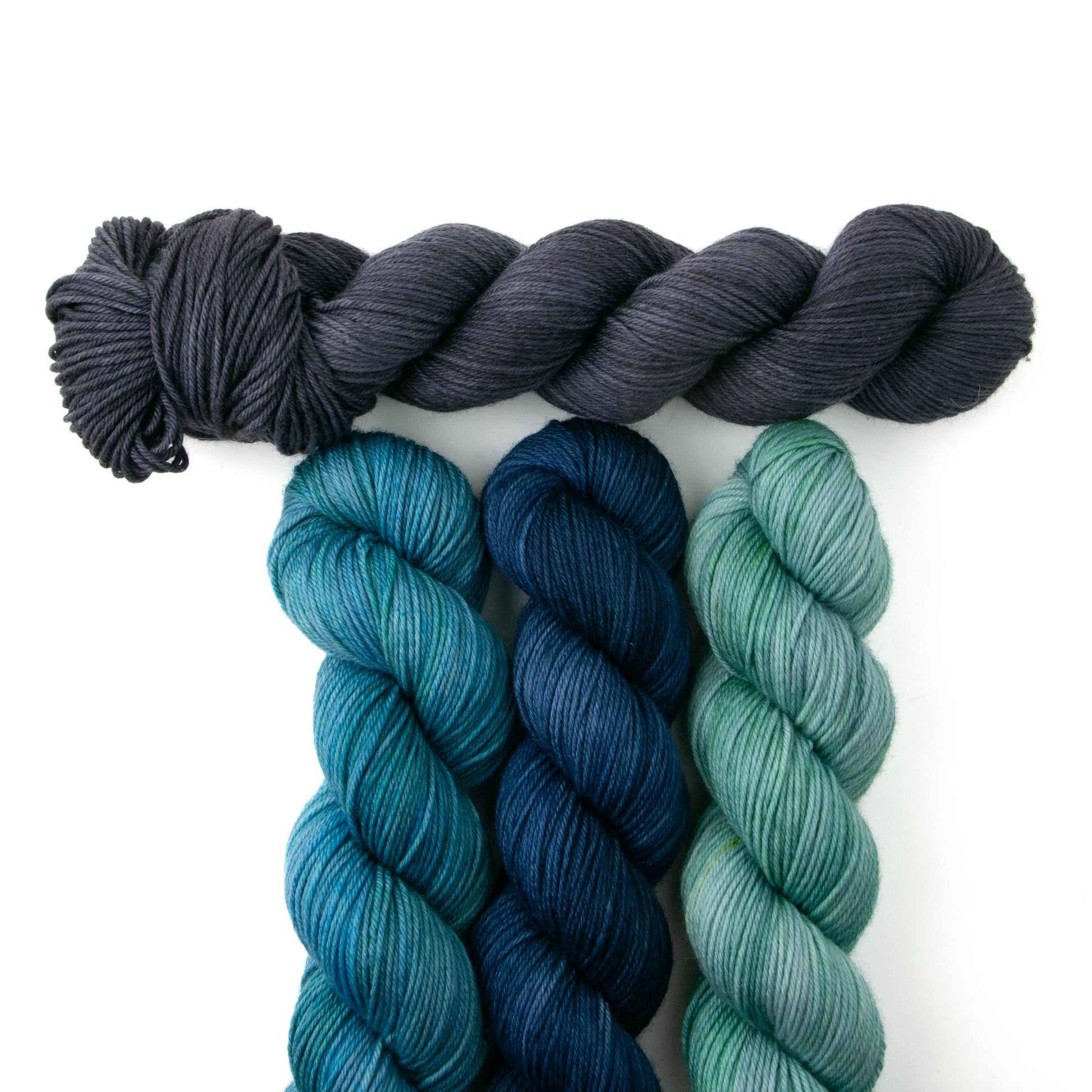 One skein of gray yarn sitting above three blue-hued skeins.