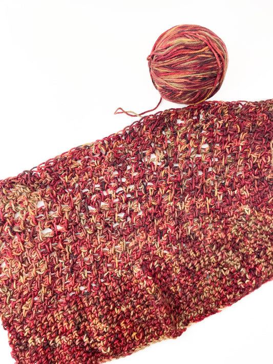 A ball of yarn and crochet swatch in red, yellow, and brown.