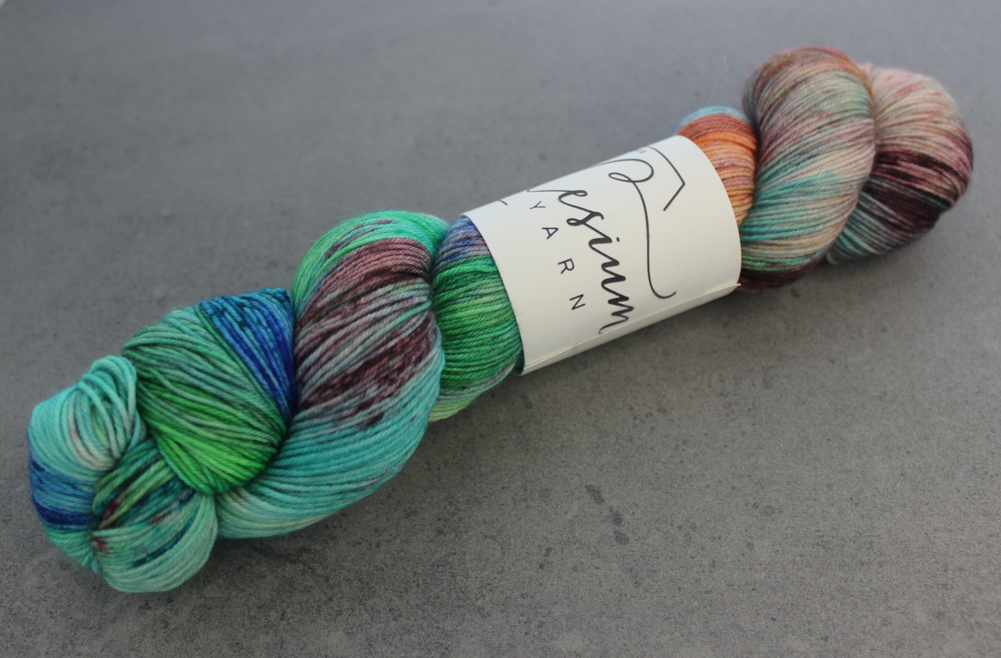 A skein of reserved multicolored hand-dyed yarn with sections of blue, aqua, green, burgundy, orange, and white.