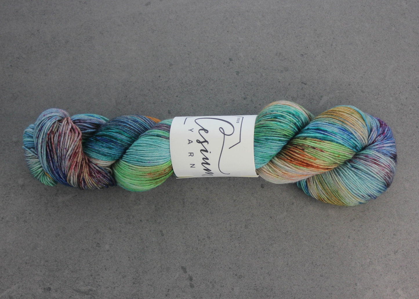 A skein of reserved multicolored hand-dyed yarn with sections of blue, aqua, green, burgundy, orange, and white.