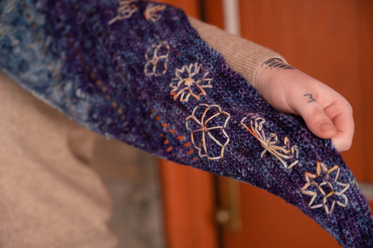 The embroidered edge of the Replenishment crochet shawl, which is embroidered with a contrasting color of yarn in various flower-inspired motifs.