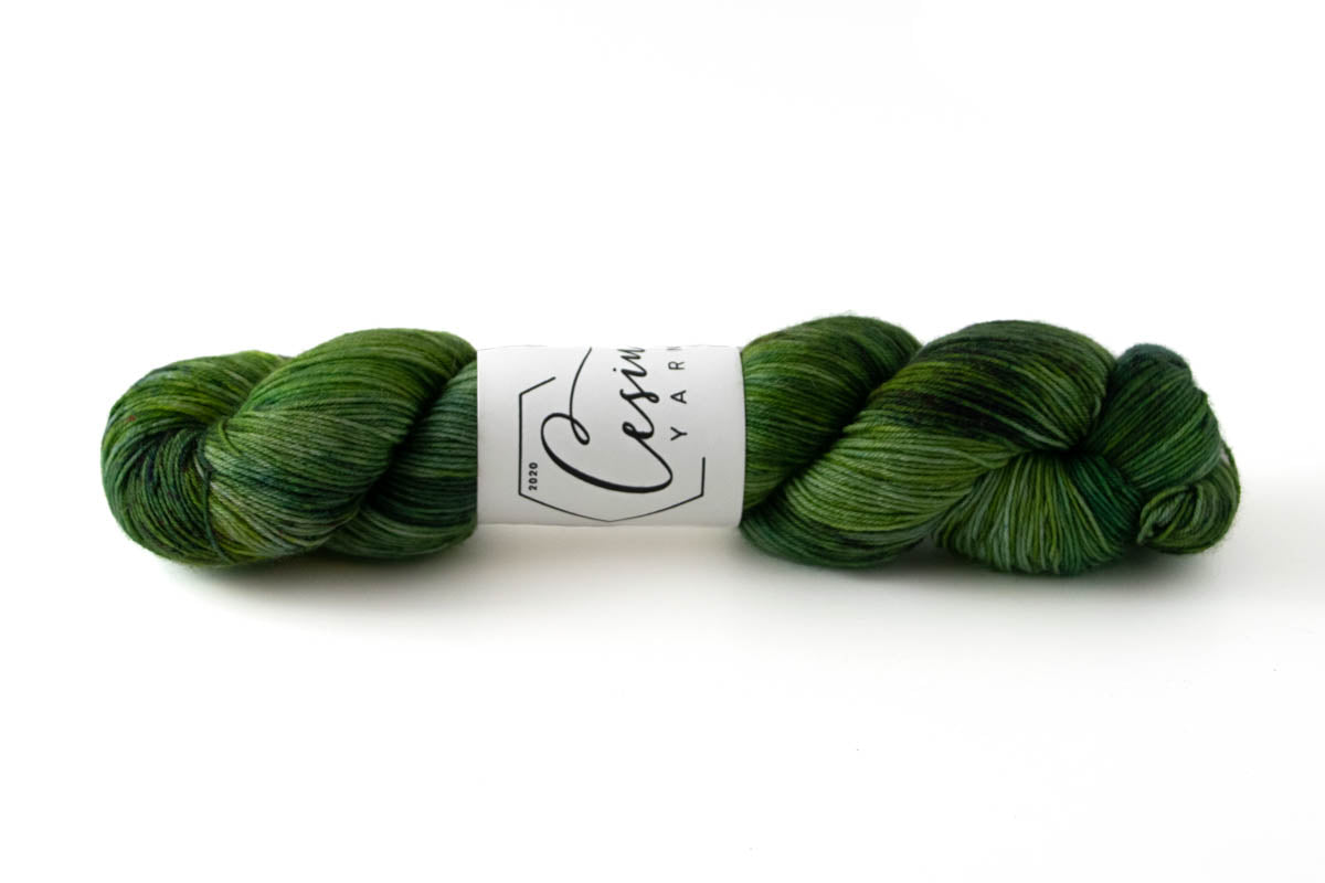 A skein of variegated hand-dyed wool yarn comprised of many shades of green.