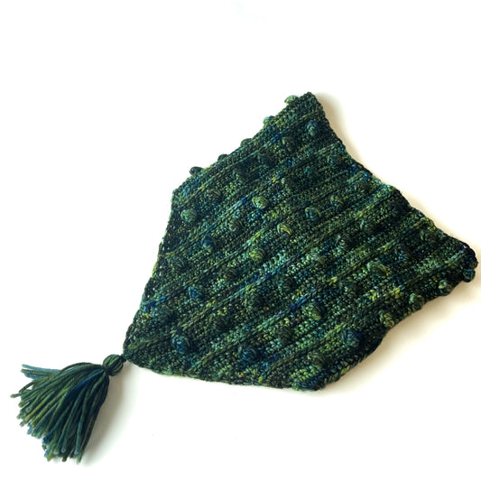A flatlay of a crochet cowl with a triangular bandana shape and a tassel, with popcorn stitch textured accents, in a blue and green variegated colorway.