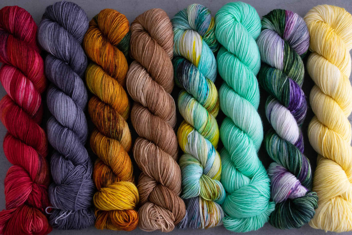 All eight skeins in the collection including red, brown, teal, yellow, purple, aqua, orange, and gray lined up together.
