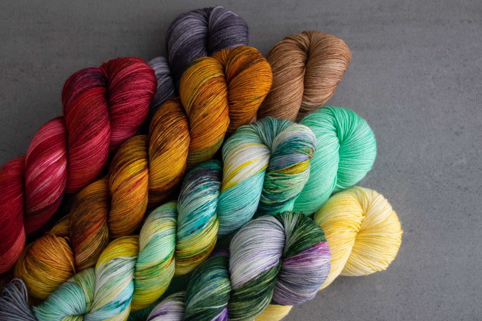 All eight skeins in the collection including red, brown, teal, yellow, purple, aqua, orange, and gray stacked on top of each other.