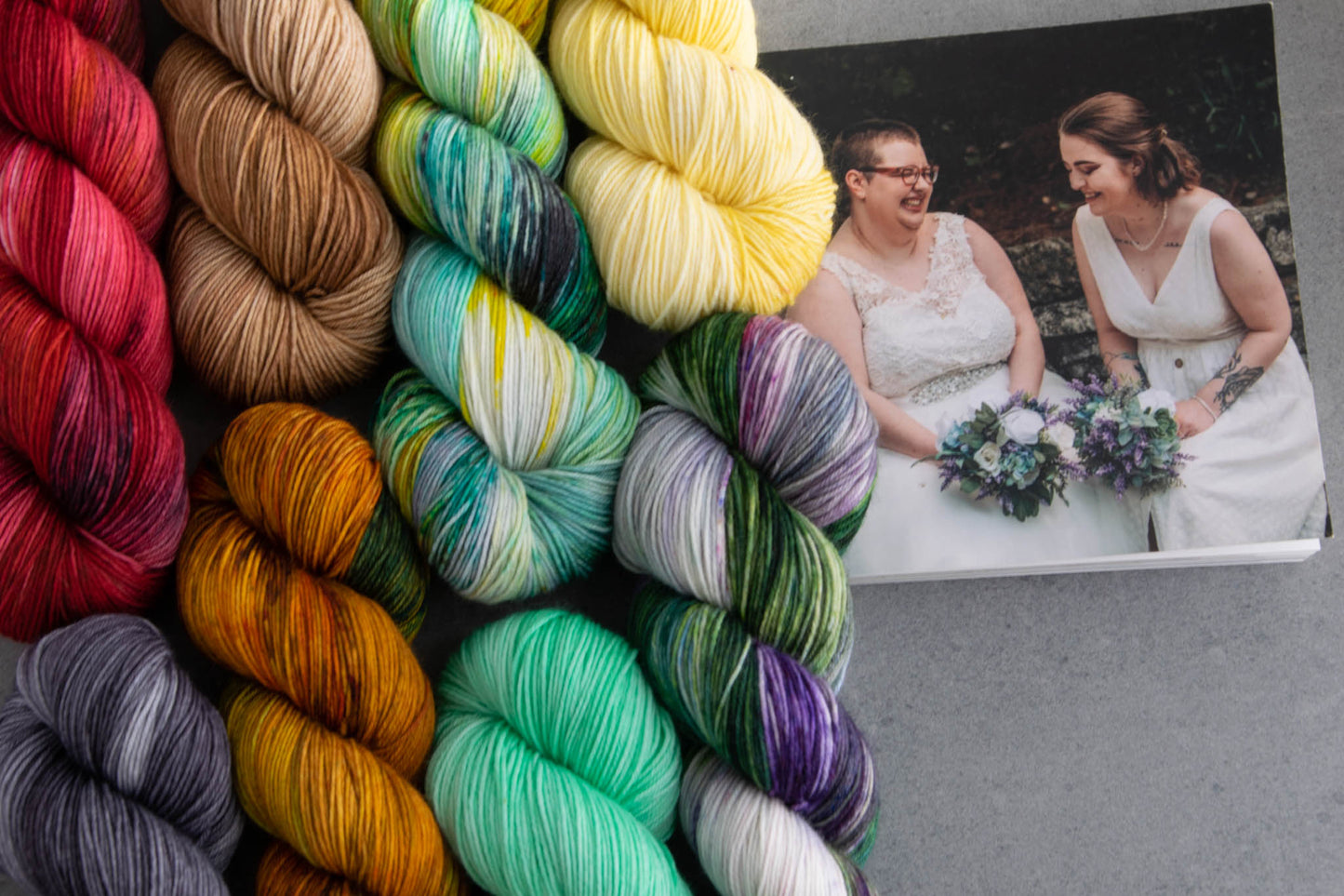 All eight skeins in the collection including red, brown, teal, yellow, purple, aqua, orange, and gray, next to a wedding photo of Cat and Penny.