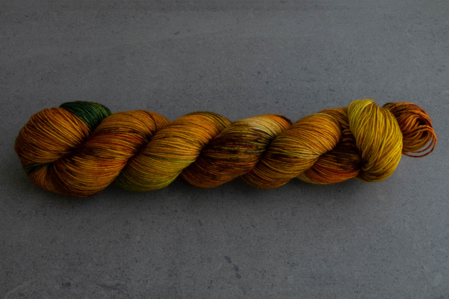 A skein of warm brown, yellow, orange, and green hand-dyed wool yarn.