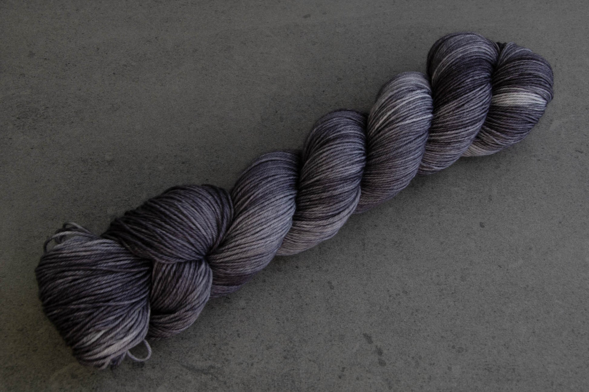 A skein of soft gray tonal hand-dyed wool yarn.