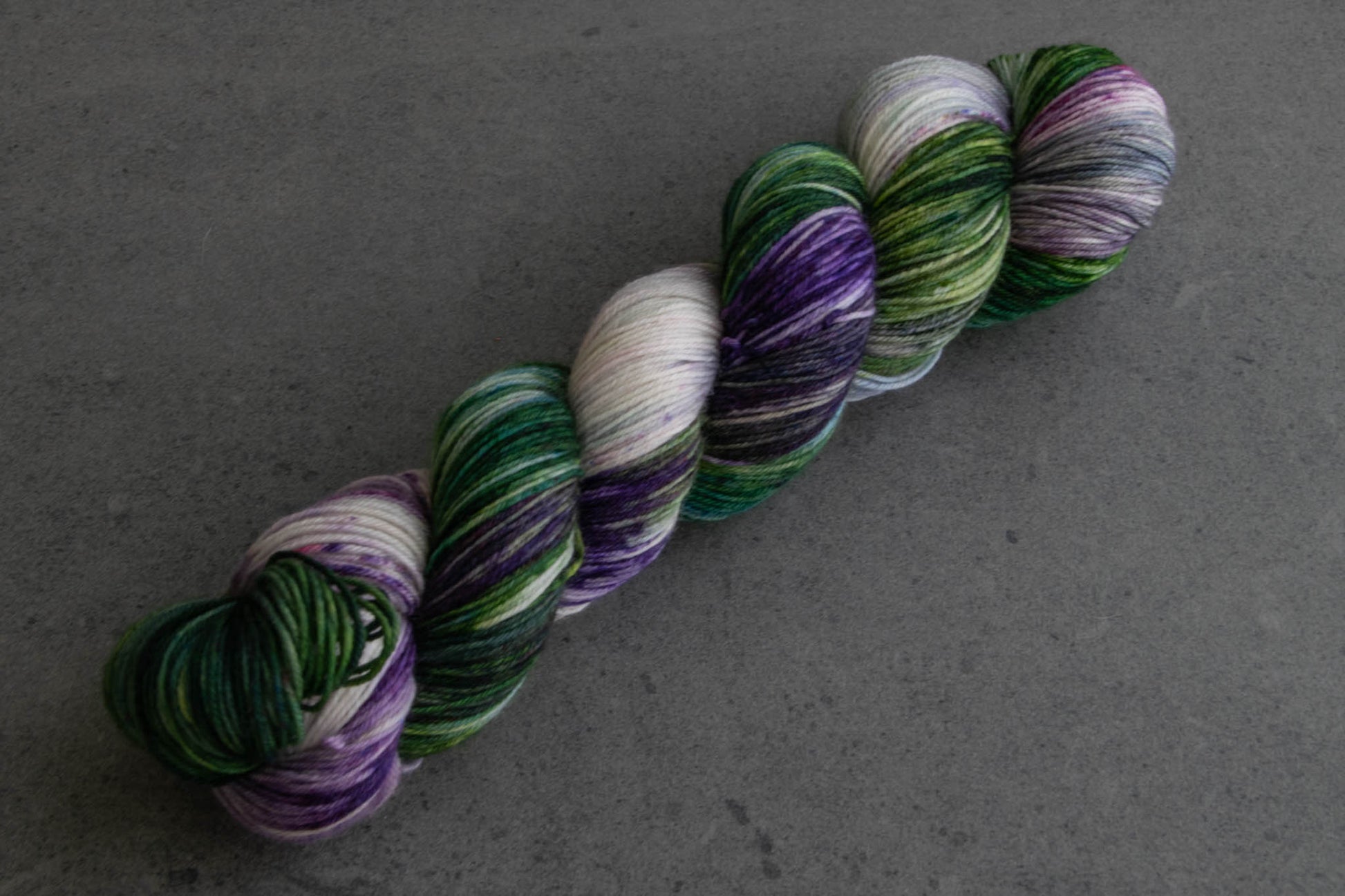 A skein of green, purple, and white variegated hand-dyed wool yarn.