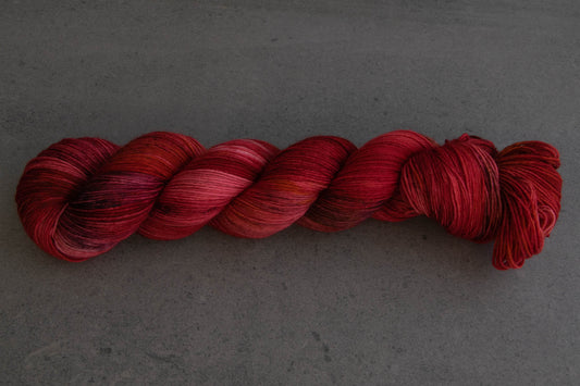 A saturated skein of red variegated hand-dyed yarn with sections of pink and plum.
