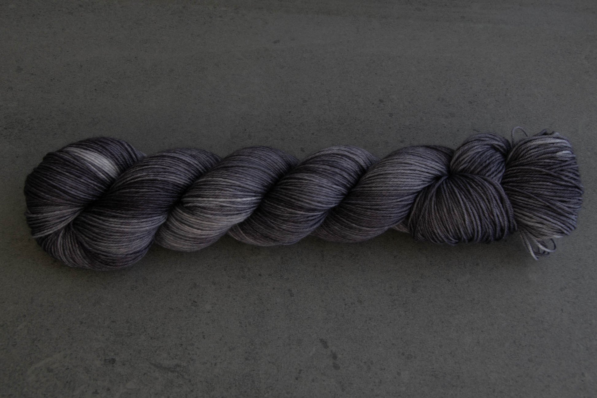 A skein of soft gray tonal hand-dyed wool yarn.
