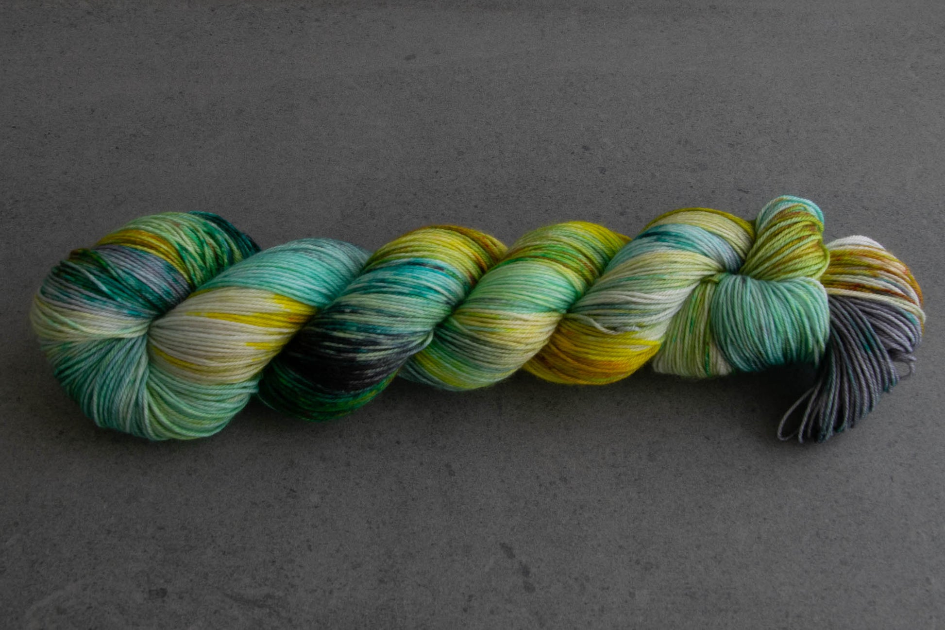 A skein of variegated aqua, yellow, green, and gray hand-dyed wool yarn.