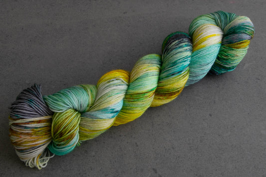 A skein of variegated aqua, yellow, green, and gray hand-dyed wool yarn.