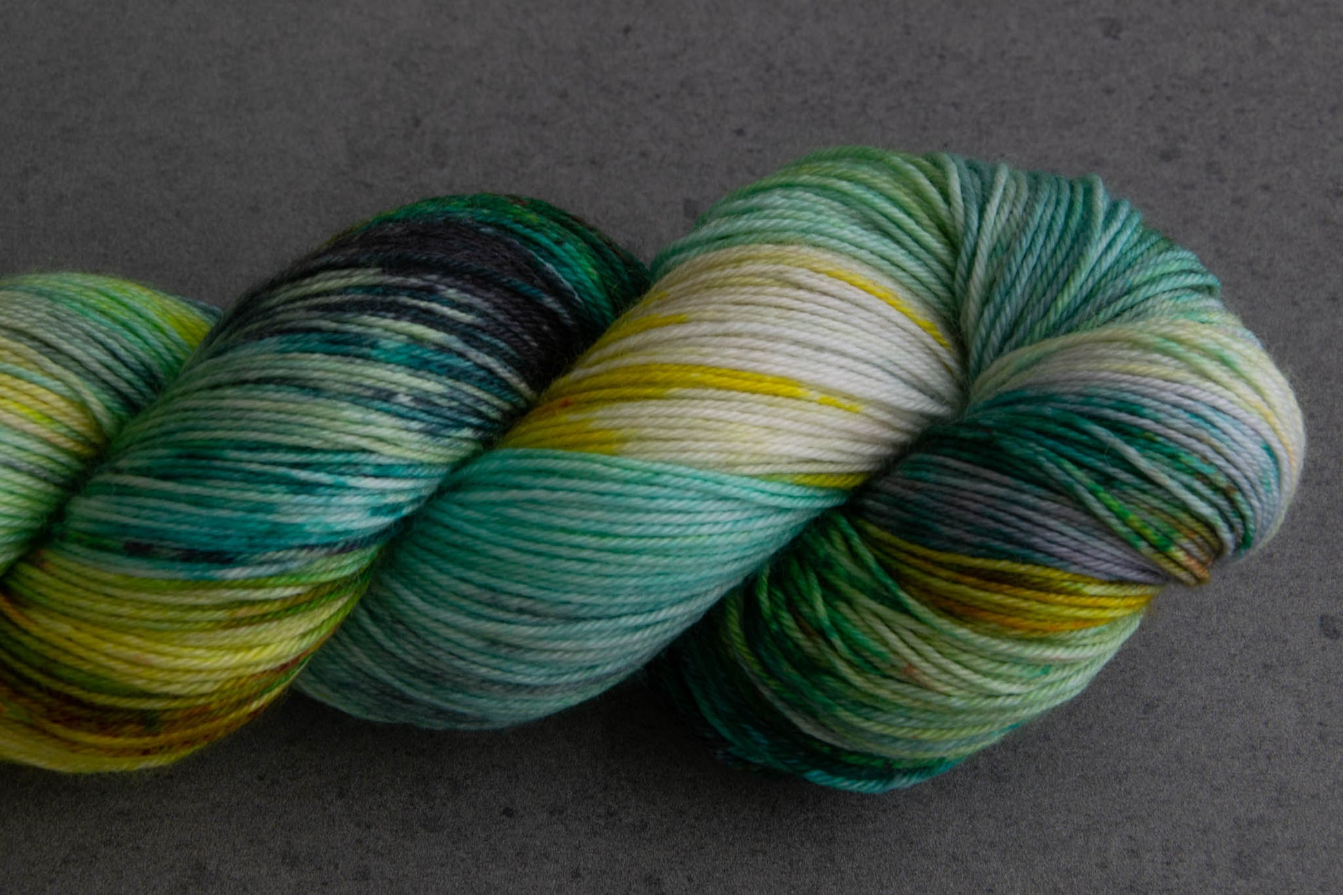 Closeup emphasizing the variegations in the skein, including sections of aqua, yellow, green, and gray.