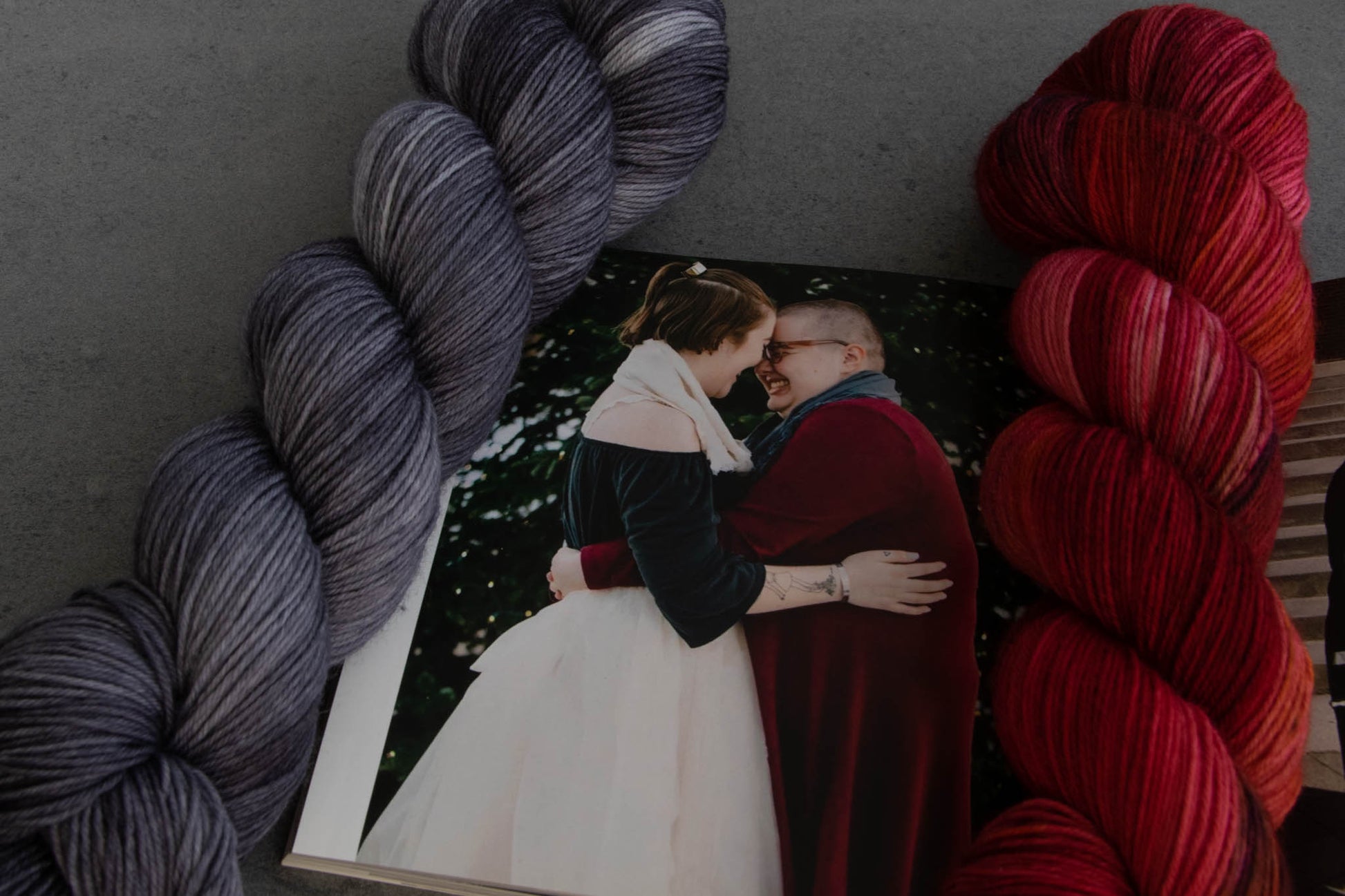 The winter colorways next to a photo of Cat and Penny. A variegated red, pink, and plum and a tonal gray.