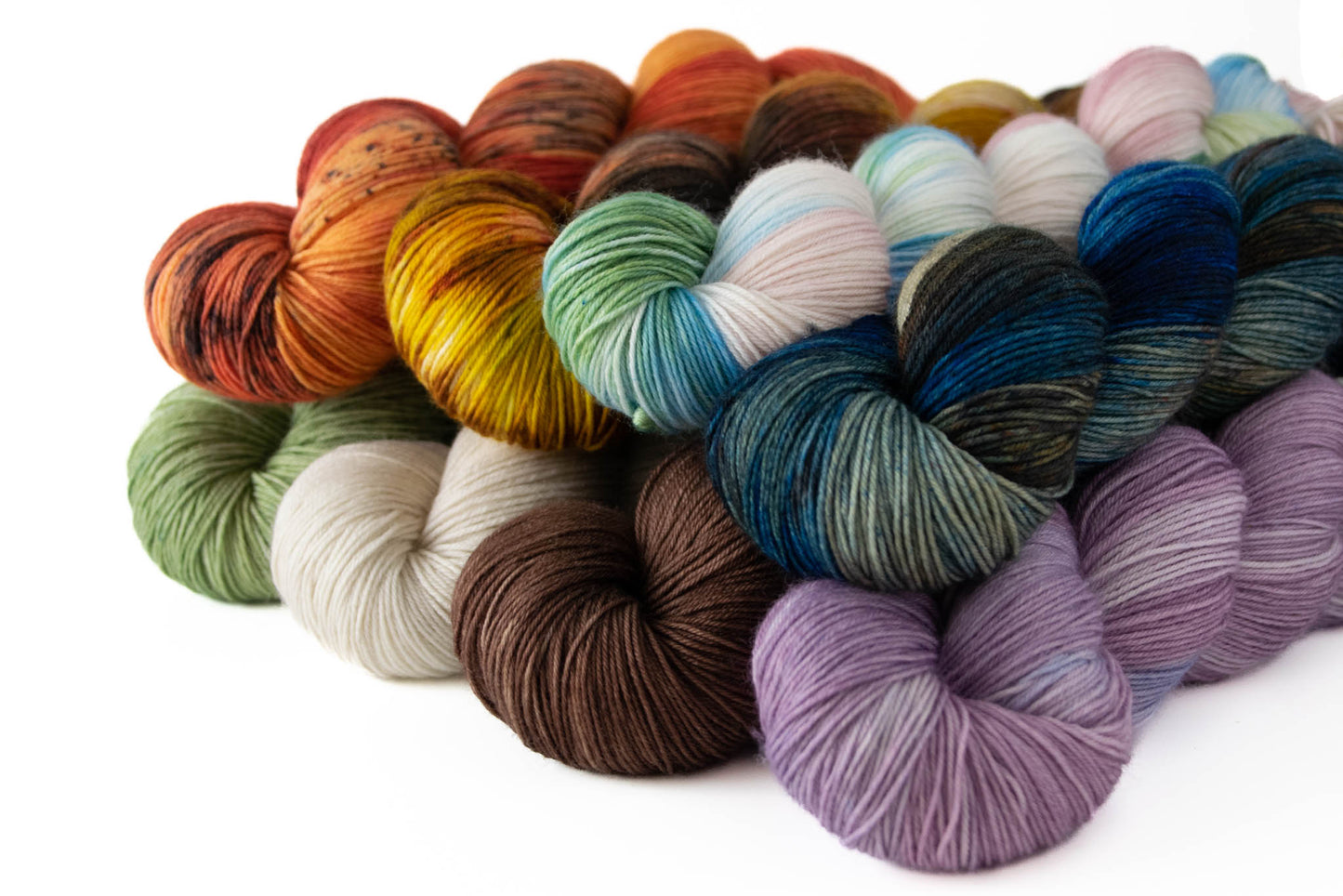 Eight skeins in the collection stacked on top of each other: red and orange; brown and yellow; green, blue, pink, and white; blue, orange, and brown; green; cream; brown; and purple.