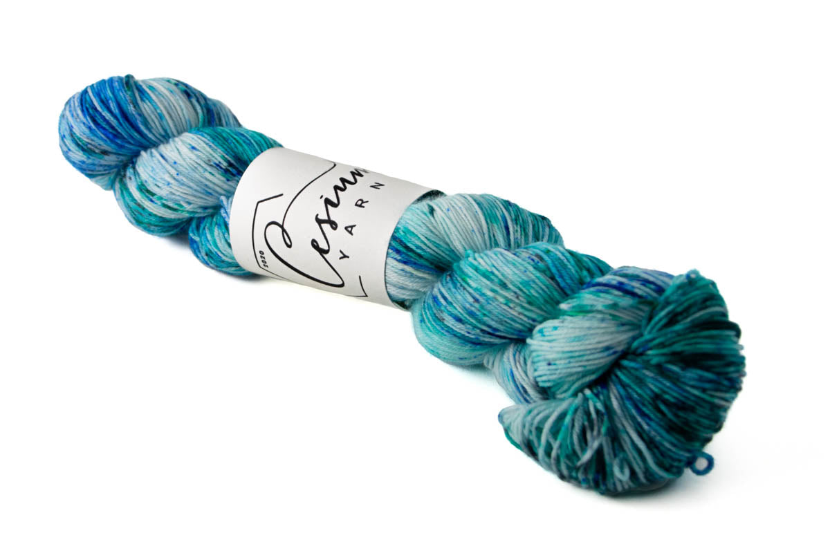A skein of variegated blue and aqua hand-dyed wool yarn with sections of icy white.