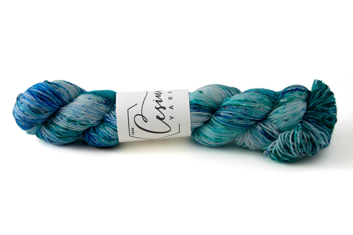 A skein of variegated blue and aqua hand-dyed wool yarn with sections of icy white.