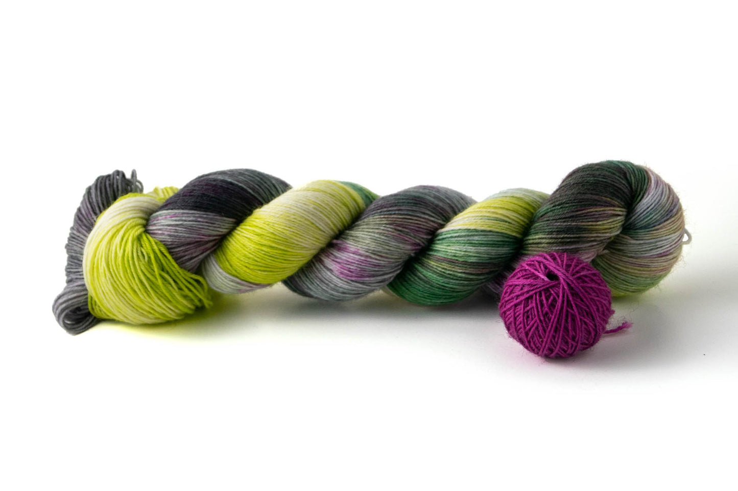 A skein of neon green, forest green, and gray hand-dyed wool yarn with pops of raspberry, next to a ball of magenta yarn.