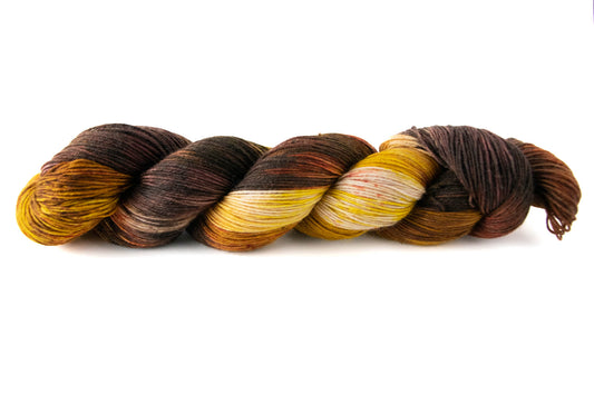 A skein of brown and yellow variegated hand dyed wool yarn with red speckles.