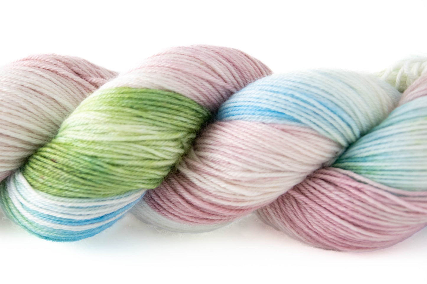 Closeup of the variegated texture of the pink, green, blue, and white hand-dyed wool yarn.