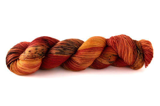 A skein of saturated red and orange variegated hand-dyed wool yarn with black speckles.