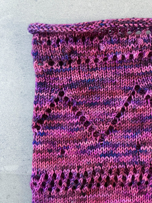 A section of a knit cowl with lace and a zig-zag pattern.