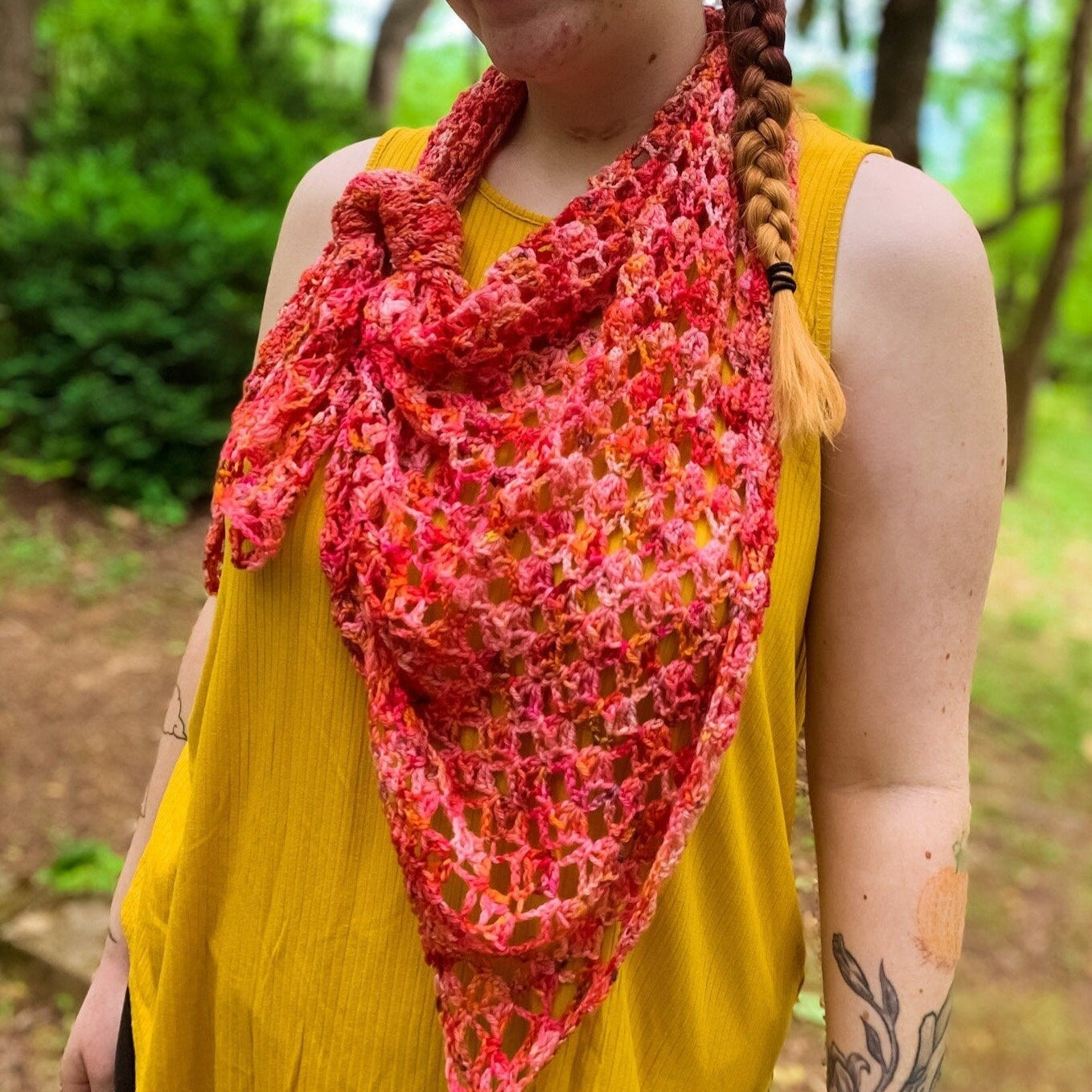 Cat (a white woman with lots of tattoos) wears a crochet shawl in the Poppy colorway. The pattern is the Hot Chili shawl by Carmen Heffernan.