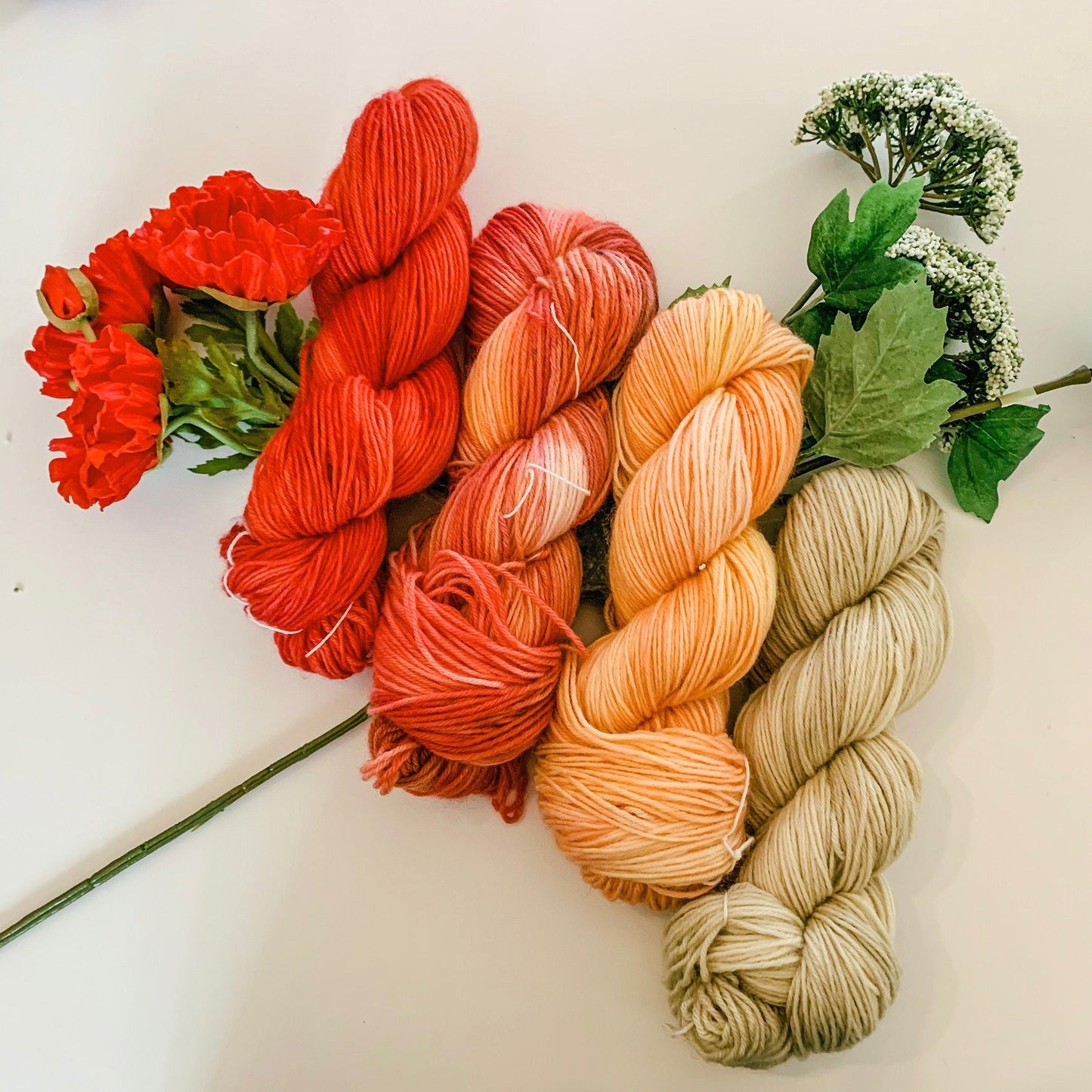 The four warm-toned colorways in the Poppy collection sitting on faux Poppy and Queen Anne's Lace flowers.