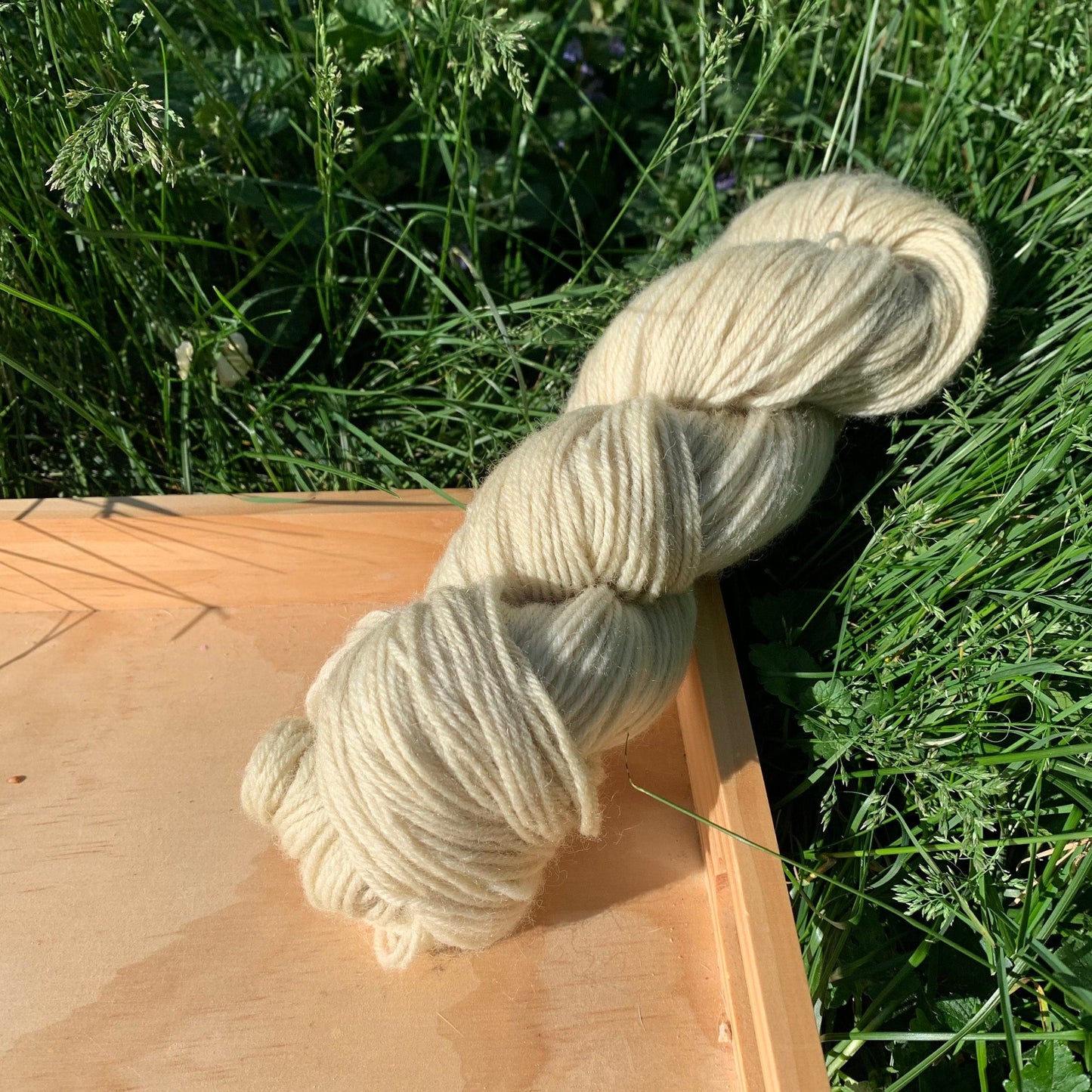 A skein of tan hand-dyed yarn on a wooden tray in grass.