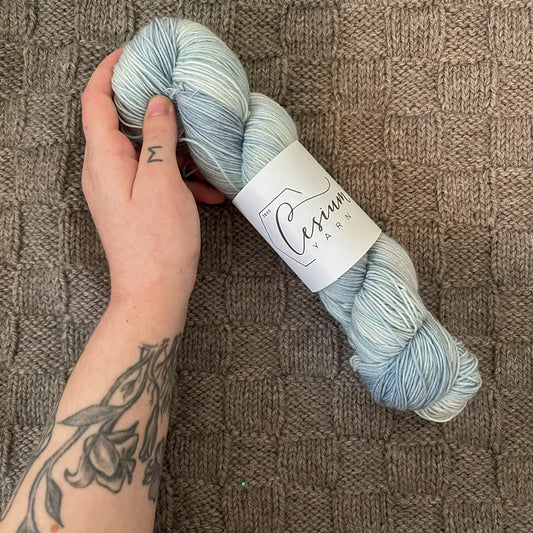 Cat holds a skein of icy blue hand-dyed wool yarn.