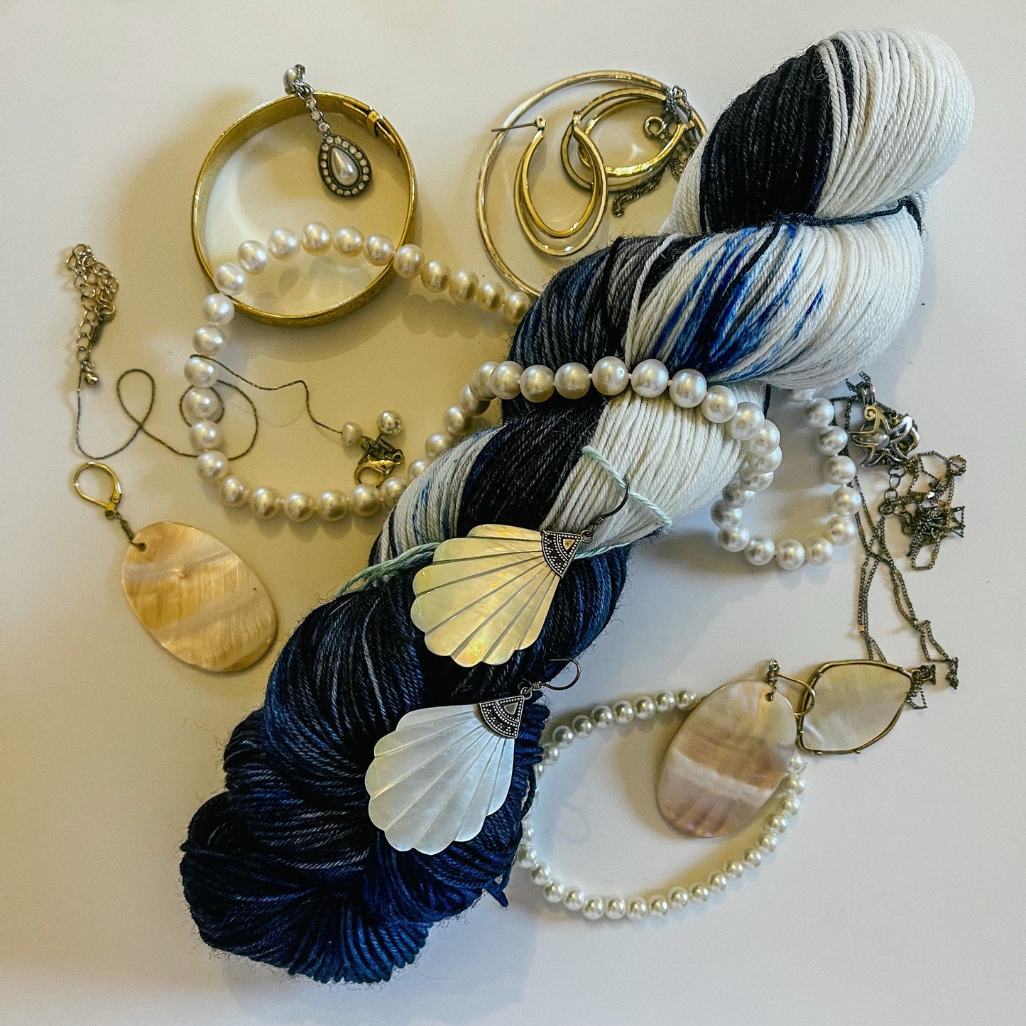 A skein of black, blue, and white variegated hand-dyed yarn surrounded by silver and pearl jewelry.