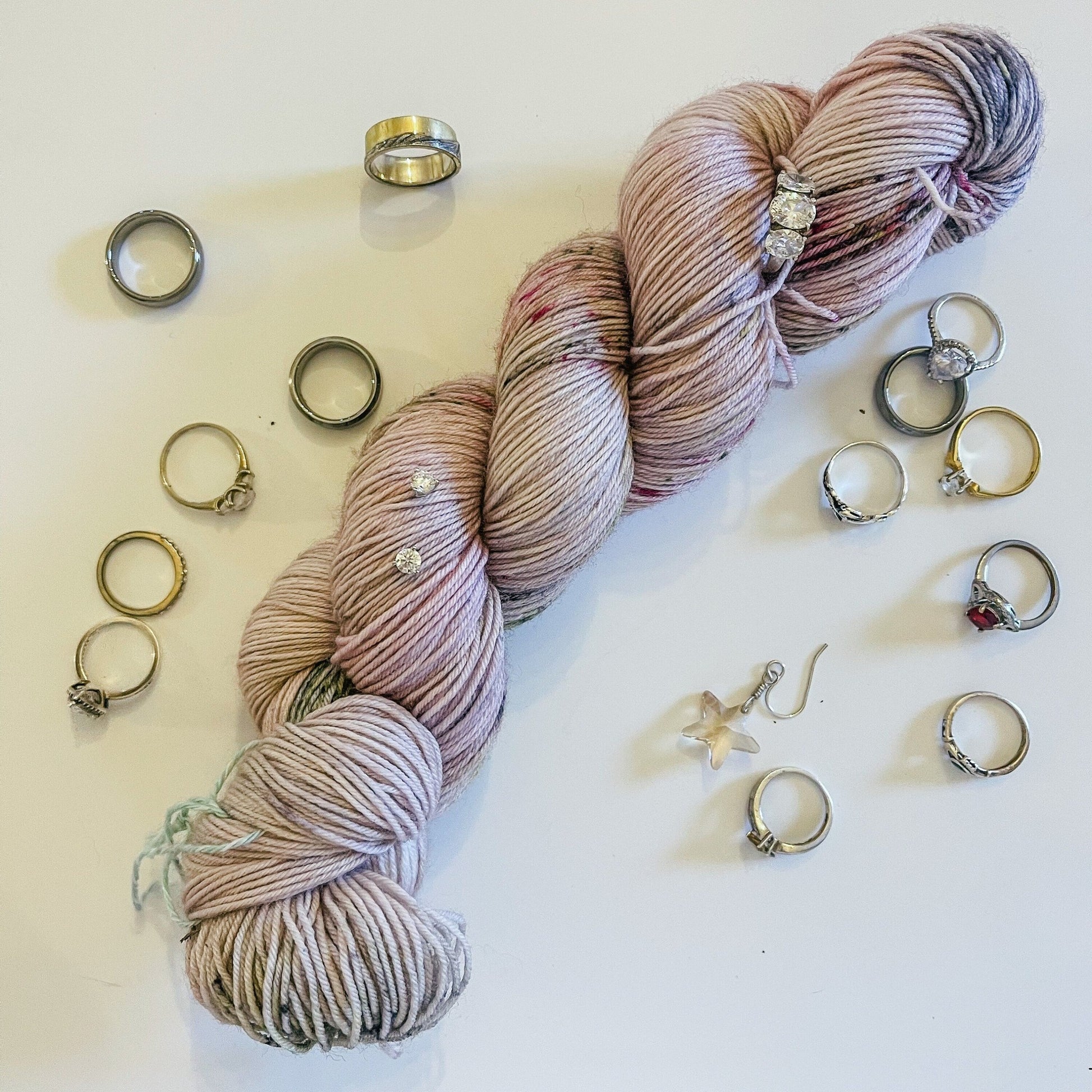 A skein of Truffle Shuffle hand-dyed yarn surrounded by jewelry, mostly rings.