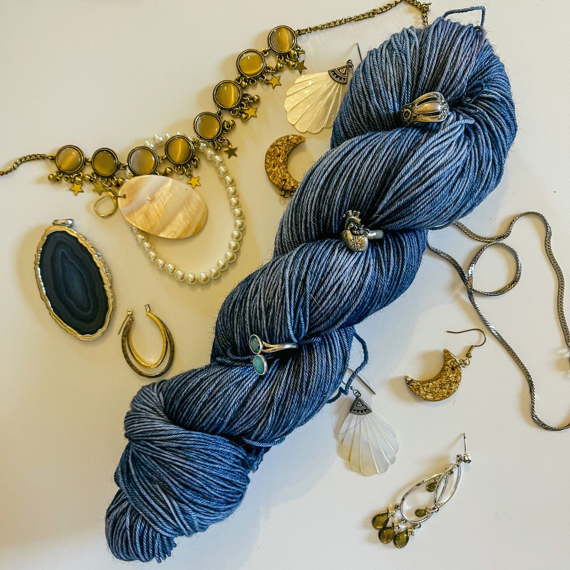 A skein of Hey Ewe Guys hand-dyed yarn surrounded by jewelry.