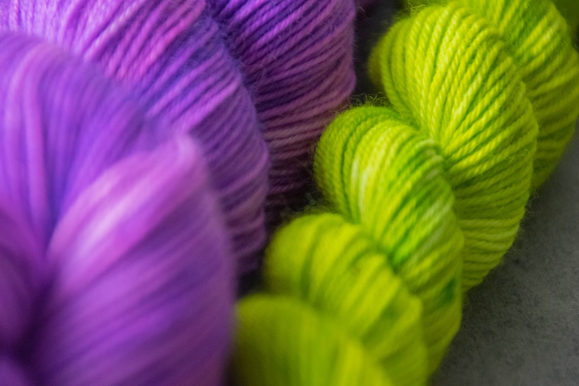 Macro shot of a skein of purple Merino wool and an electric green mini.