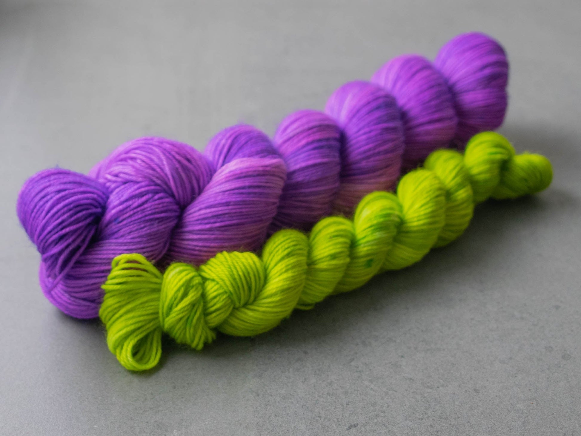 Full view of a large skein of purple Merino wool and a mini skein of electric green.