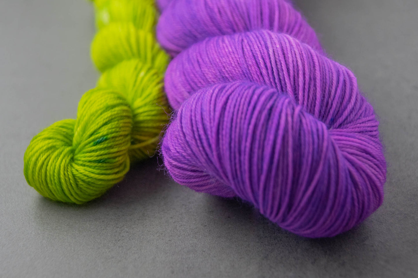 Close view of a skein of purple Merino wool and a mini in electric green.