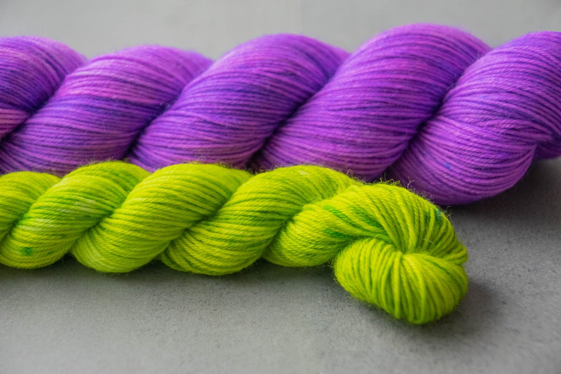 A skein of purple Merino wool yarn next to an electric green mini.