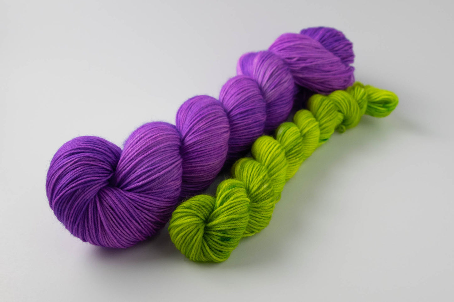 A skein of purple Merino wool and a mini skein of electric green on a white background.