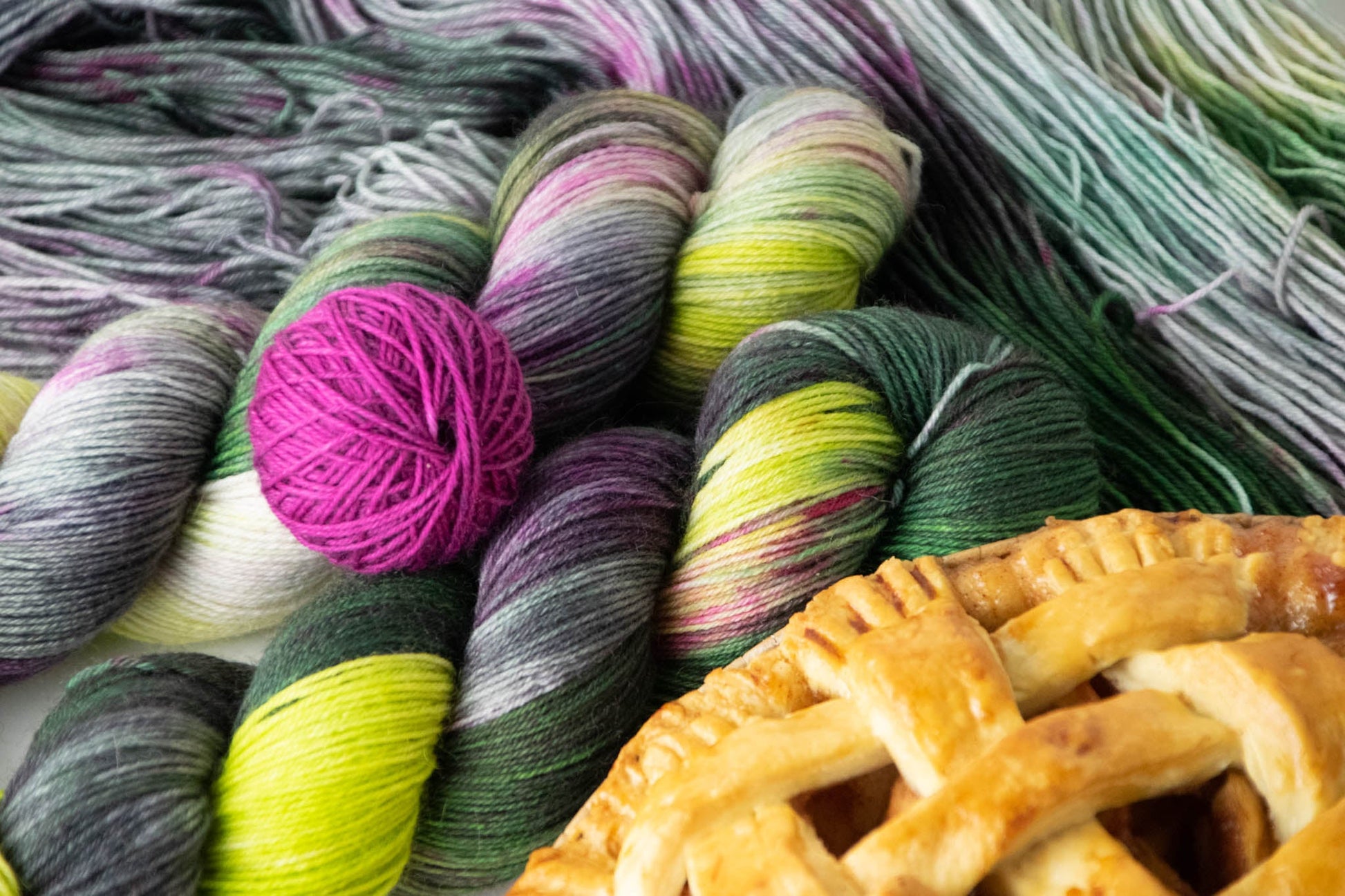 A pile of Python variegated yarn with a ball of Scratch magenta yarn and a golden pie crust in the foreground.